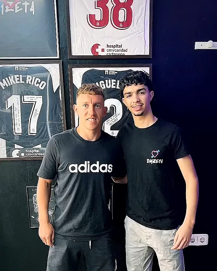 Cliente y barbero delante de la pared de camisetas